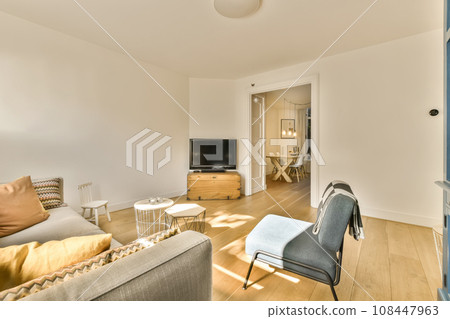 a living room with white walls and hardwood flooring, including a grey sofa set in the center of the room a living room with white walls and hardwood flooring, including a grey sofa set in the center of the room 108447963