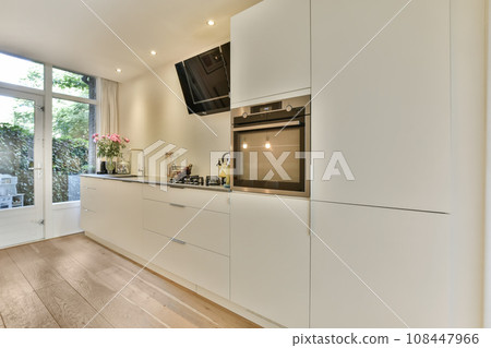 a kitchen with wood flooring and white cabinets in the center of the image is an open door leading to a patio 108447966