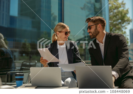 Business colleagues working with documents and use laptop sitting outside of office on cafe terrace 108448069