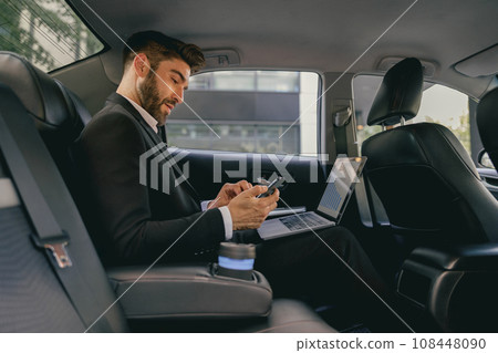 Busy male analyst working on laptop and use mobile phone while going to airport by car 108448090