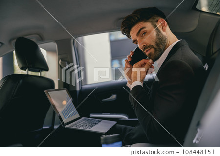 Busy entrepreneur working on laptop and talking on phone while going to airport by car 108448151
