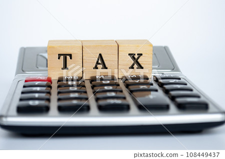 Tax word on wooden cubes on top of a calculator with white background. Tax and financial concept. Tax word on wooden cubes on top of a calculator with white background. Tax and financial concept. 108449437