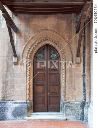 Close-up of a weathered wooden door in a brick wall. The door has a metal handle and a stained glass window above Close-up of a weathered wooden door in a brick wall. The door has a metal handle and a stained glass window above 108450284
