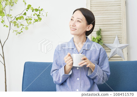 A woman in pajamas drinking a hot drink in the living room A woman in pajamas drinking a hot drink in the living room 108451570