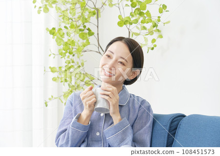一個穿著睡衣的女人在客廳裡喝著熱飲 108451573