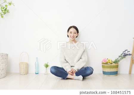 Portrait of a smiling woman sitting in the living room, full body, looking at camera, with copy space 108451575
