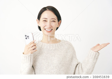 A woman holding a smartphone and pointing to the right side with her palm, white background 108451639