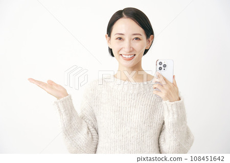 一位女士拿著智慧型手機，用手掌、白色背景指著左側 108451642