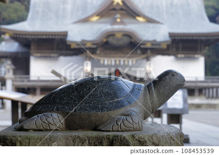 A stone statue of a lucky turtle with the worship hall of Sakatsurai Isomae Shrine, famous for its large lottery winnings, in the background. 108453539