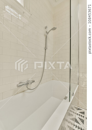 a white bathtub in a bathroom with tiled walls and black and white tiles on the floor, there is a glass shower door 108453671