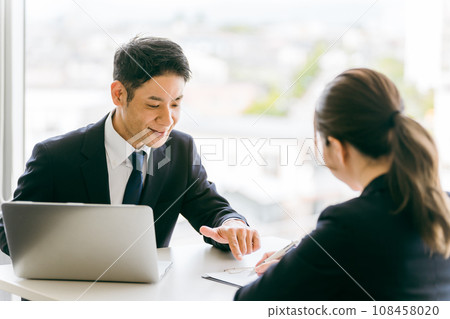 A woman listens to a businessman in a suit who explains documents, provides consultation, and provides guidance. A woman listens to a businessman in a suit who explains documents, provides consultation, and provides guidance. 108458020