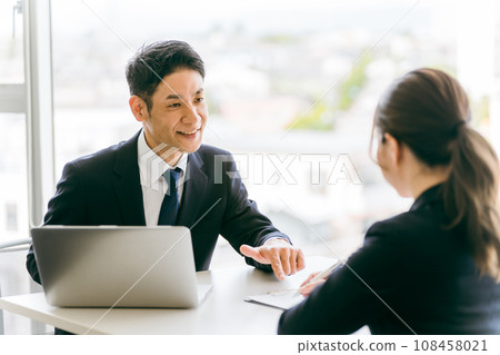 A woman listens to a businessman in a suit who explains documents, provides consultation, and provides guidance. A woman listens to a businessman in a suit who explains documents, provides consultation, and provides guidance. 108458021