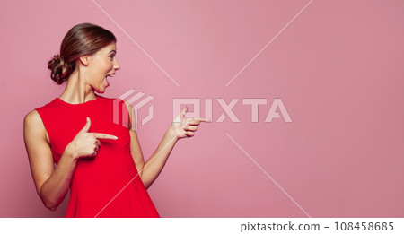 Happy beautiful woman pointing finger against pink studio wall banner background 108458685