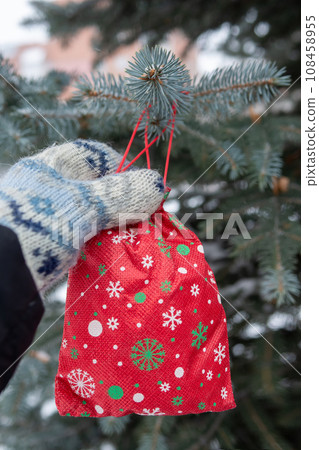 red Christmas gift is hanging on pine tree outdoors. red Christmas gift is hanging on pine tree outdoors. 108458955