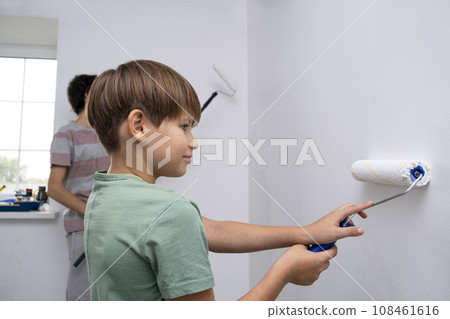 children paint the wall with a roller. teenagers spend time together helping to make repairs. 108461616