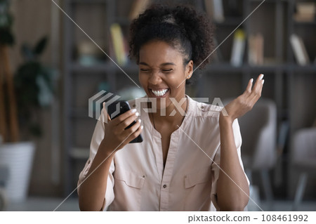 Happy young Black woman reading text on mobile phone screen Happy young Black woman reading text on mobile phone screen 108461992