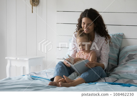 Mum and little daughter read book together in bed 108462230