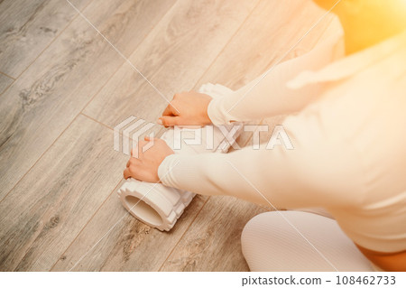 Adult athletic woman, in white bodysuit, performing fascia exercises on the floor - caucasian woman using a massage foam roller - a tool to relieve tension in the back and relieve muscle pain - the Adult athletic woman, in white bodysuit, performing fascia exercises on the floor - caucasian woman using a massage foam roller - a tool to relieve tension in the back and relieve muscle pain - the 108462733