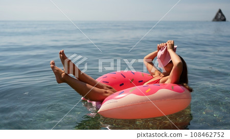 Summer vacation woman in hat floats on an inflatable donut mattress. Happy woman relaxing and enjoying family summer travel holidays travel on the sea. 108462752