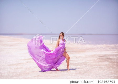 Woman pink salt lake. Against the backdrop of a pink salt lake, a woman in a long pink dress takes a leisurely stroll along the white, salty shore, capturing a wanderlust moment. Woman pink salt lake. Against the backdrop of a pink salt lake, a woman in a long pink dress takes a leisurely stroll along the white, salty shore, capturing a wanderlust moment. 108462793