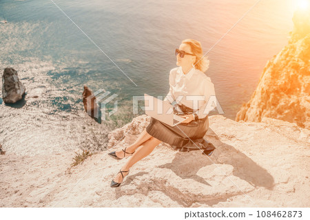 Business woman on nature in white shirt and black skirt. She works with an iPad in the open air with a beautiful view of the sea. The concept of remote work. Business woman on nature in white shirt and black skirt. She works with an iPad in the open air with a beautiful view of the sea. The concept of remote work. 108462873