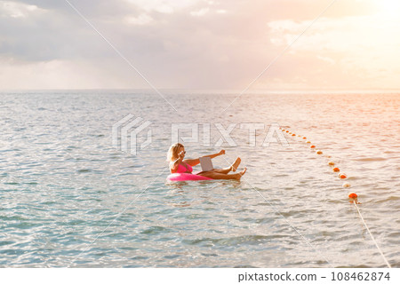 Woman works on laptop in sea. Freelancer, blond woman in sunglases floating on an inflatable big pink donut with a laptop in the sea at sunset. People summer vacation rest lifestyle concept. Woman works on laptop in sea. Freelancer, blond woman in sunglases floating on an inflatable big pink donut with a laptop in the sea at sunset. People summer vacation rest lifestyle concept. 108462874