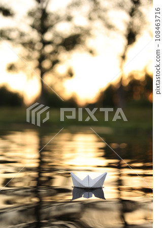 A paper boat is floating on the waves in the water at a beautiful sunset. Origami ship Sailing. The concept of a dream, future, childhood, freedom or hope. A paper boat is floating on the waves in the water at a beautiful sunset. Origami ship Sailing. The concept of a dream, future, childhood, freedom or hope. 108463716