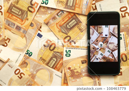 Money paper 50 euro banknotes on the background of a smartphone screen, the concept of business, investment and income growth. Mobile banking and finance concept Money paper 50 euro banknotes on the background of a smartphone screen, the concept of business, investment and income growth. Mobile banking and finance concept 108463779
