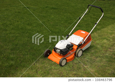 Top view of modern orange-grey electric lawn mower cutting bright lush green grass. Gardening work tools. Rotary lawn mower machine on lawn. Professional lawn care service. Place for text 108463796