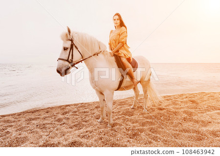 A white horse and a woman in a dress stand on a beach, with the A white horse and a woman in a dress stand on a beach, with the 108463942