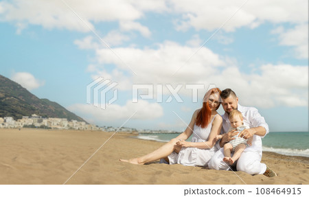 Happy family on vacation sitting on a sand beach with a baby son 108464915
