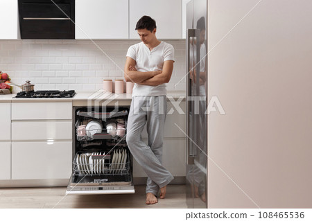 handsome husband man using dishwasher and washing dishes in white modern kitchen. copy space handsome husband man using dishwasher and washing dishes in white modern kitchen. copy space 108465536