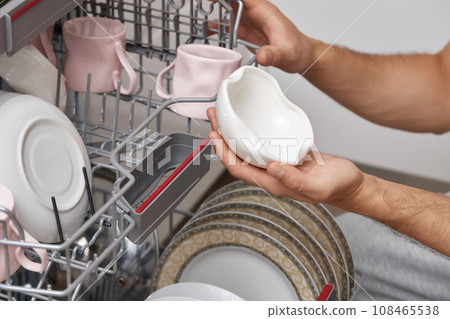 male hand unloading plates from open automatic dishwasher machine with clean utensils inside in kitchen. male hand unloading plates from open automatic dishwasher machine with clean utensils inside in kitchen. 108465538