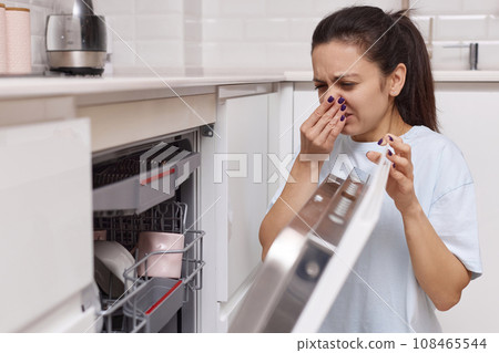 woman smells strange and terrible smell coming from dishwasher machine in kitchen 108465544