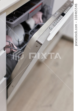 Open built-in dishwasher machine with clean cutlery, dishes, plates in white modern kitchen Open built-in dishwasher machine with clean cutlery, dishes, plates in white modern kitchen 108465546