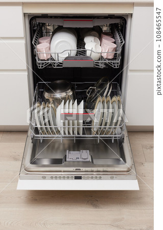 Open built-in dishwasher machine with clean cutlery, dishes, plates in white modern kitchen. front view Open built-in dishwasher machine with clean cutlery, dishes, plates in white modern kitchen. front view 108465547