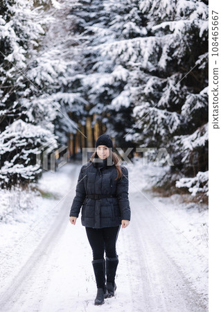 Beautiful girl in black winter clothes walking in snowy forest. Christmas Hollidays  108465667