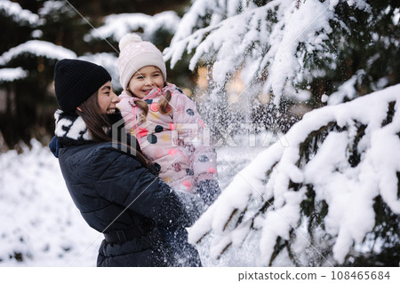 Happy mom and daughter shake off the snow from a Christmas tree branch 108465684