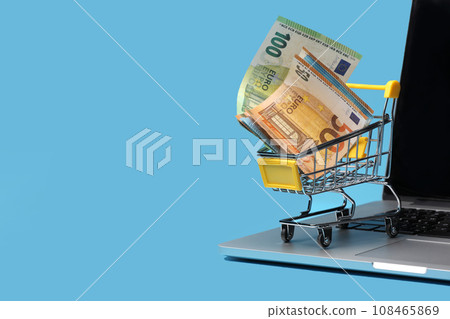shopping cart with euro banknotes inside on laptop on blue background, shopping online concept. shopping cart with euro banknotes inside on laptop on blue background, shopping online concept. 108465869