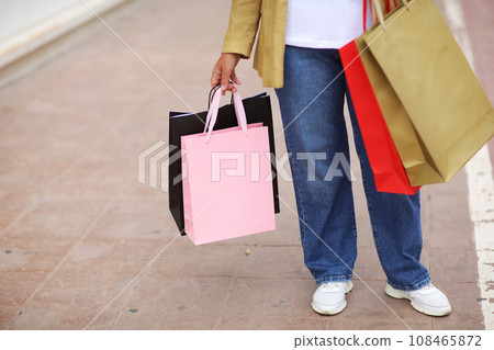 Cropped portrait of unrecognisable woman with colourful shopping bags on urban shopping mall background. Purchases, black friday, discounts, sale concept. Online shopping concept, Seasonal Sales. Cropped portrait of unrecognisable woman with colourful shopping bags on urban shopping mall background. Purchases, black friday, discounts, sale concept. Online shopping concept, Seasonal Sales. 108465872