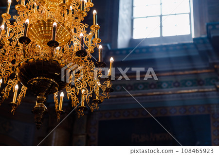 Big bronze chandelier with electric candles in cathedral christian church. daylight from the window in the church. selective focus Big bronze chandelier with electric candles in cathedral christian church. daylight from the window in the church. selective focus 108465923