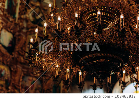 gold-plated chandelier hangs in the old church near the icons. Modern lamps are like candles. 108465932