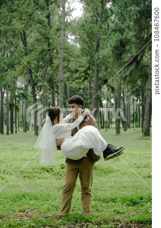 asian young man is carring girl with smile face on pine tree background asian young man is carring girl with smile face on pine tree background 108467600