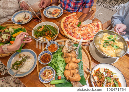 Dinner meal with Thai food as fried fish with spicy sauce, Spicy vegetable salad, Local vegetables with chili sauce and pizza bacon ham cheese on wooden table 108471764
