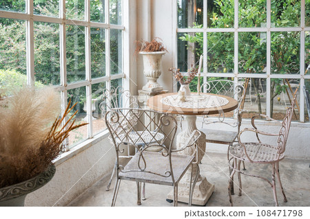Vintage table and chairs by the window among the tropical garden in coffee shop Vintage table and chairs by the window among the tropical garden in coffee shop 108471798