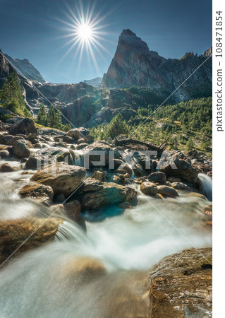 Swiss Alps of Wetterhorn peak with sunburst shine and waterfall flowing in sunny day at Reichenbach, Rosenlaui, Switzerland Swiss Alps of Wetterhorn peak with sunburst shine and waterfall flowing in sunny day at Reichenbach, Rosenlaui, Switzerland 108471854
