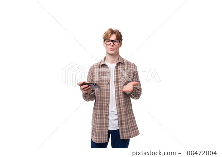 a young european man with red short hair and glasses is dressed in a plaid shirt holding a phone in a young european man with red short hair and glasses is dressed in a plaid shirt holding a phone in 108472004