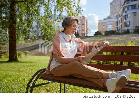 Senior mature woman reading newspaper at park on summer day 108472265