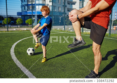 Dad and son doing physical workout and warming legs up before football training 108472292