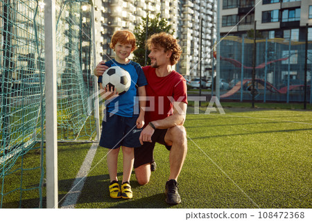 Happy father and little son standing near football gate 108472368